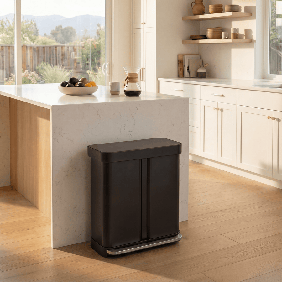 Simplehuman's Matte Black 58L Step Recycler in a simple, classic styled kitchen with white and marble accents and a few house hold appliances on the shelves and countertop.