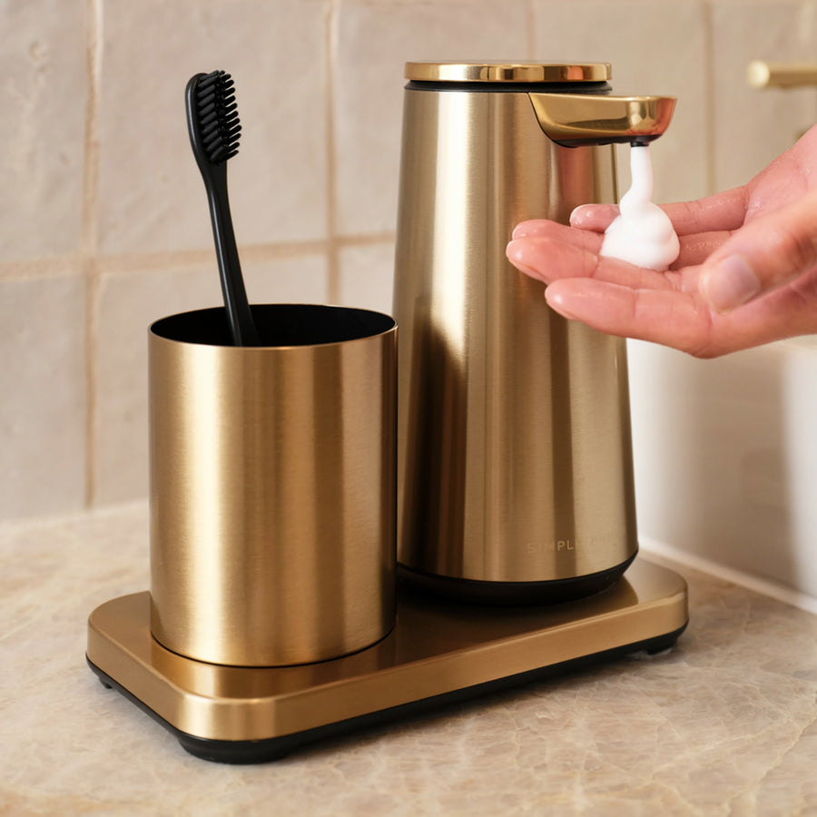 Lifestyle view: Simplehuman Brushed Brass Foam Sensor Pump and removable Cup holding a toothbrush, touch-free operation.