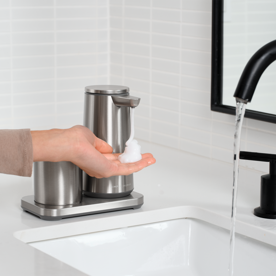 Simplehuman Brushed Stainless Steel touch-free Foam Pump and Cup set dispensing soap into a hand in the bathroom.