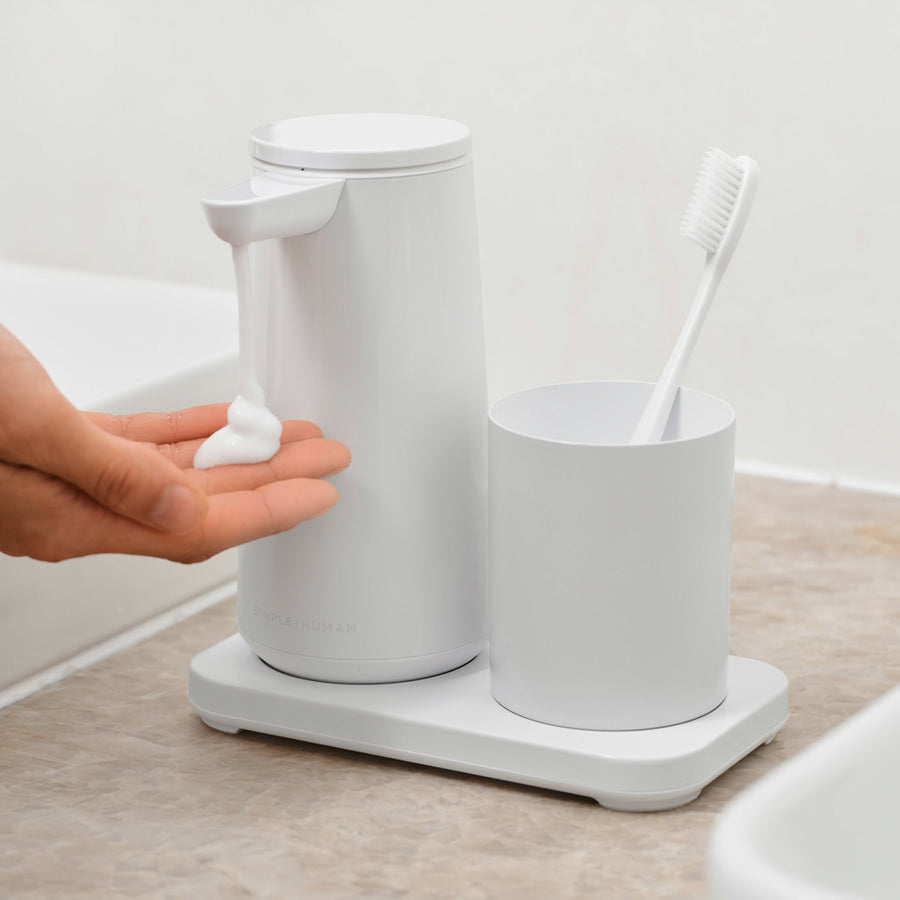 Lifestyle view: Simplehuman White touch-free Foam Sensor Pump and Cup set dispensing foam soap into a hand, used in a bathroom setting.